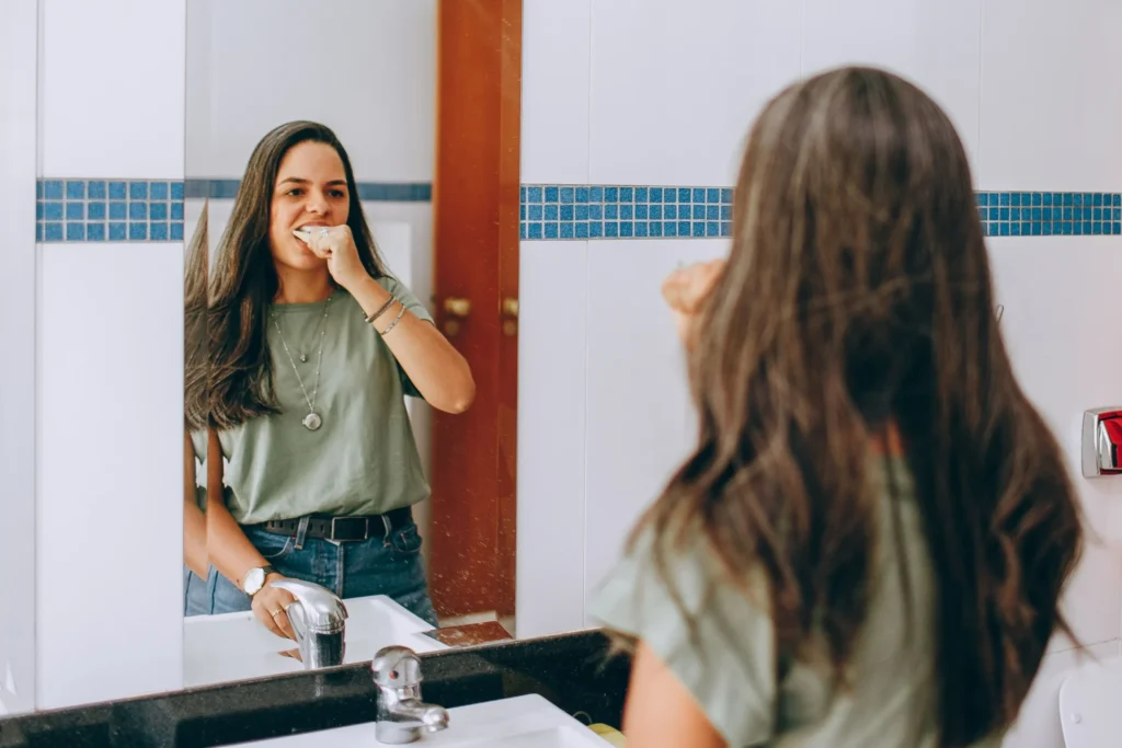 Person brushing their teeth in a bathroom mirror as part of daily oral care.
